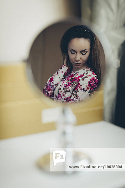 Reflektion der jungen Frau im Blumenkleid im Spiegel
