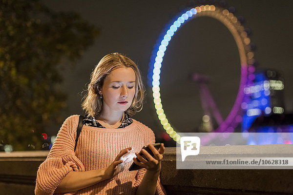 UK  London  young woman looking at her smartphone with London Eye in the background
