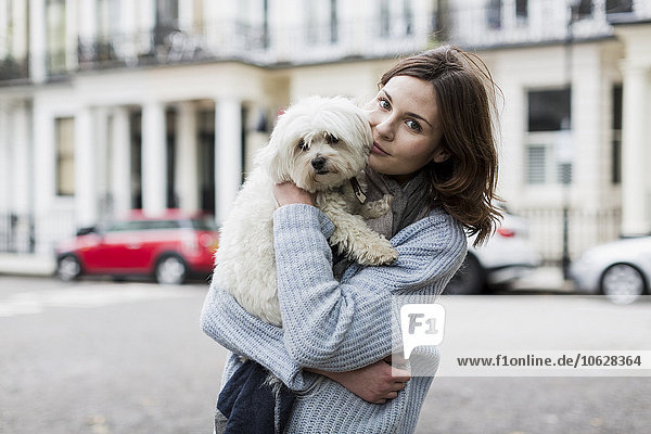 Porträt einer jungen Frau  die ihren Hund auf den Armen hält.