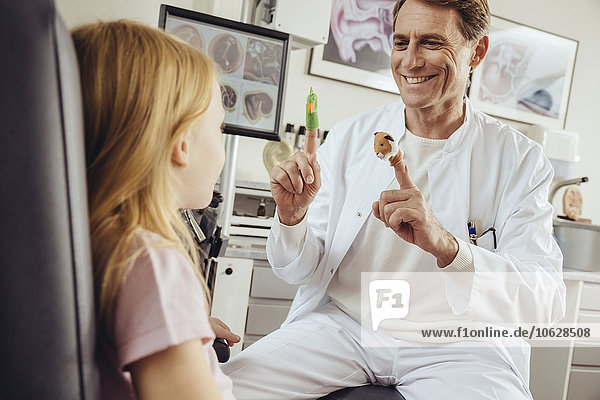 Doctor playing with little girl with in ENT practice  using finger puppets