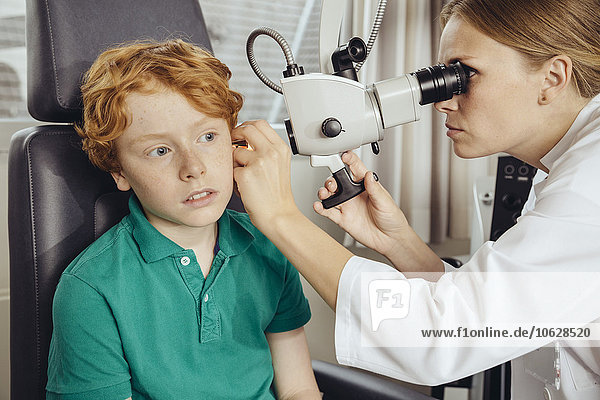 Female doctor examining little boy with microscope