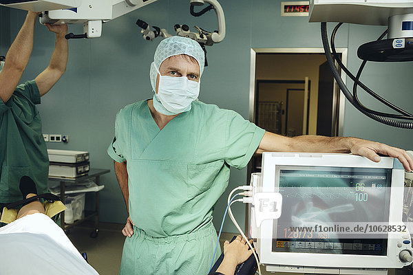 Porträt eines Chirurgen im Operationssaal  der sich an ein Anästhesiegerät lehnt.