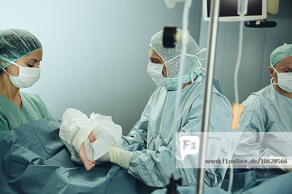 Chirurg übergibt Neugeborenes an OP-Schwester nach Kaiserschnitt