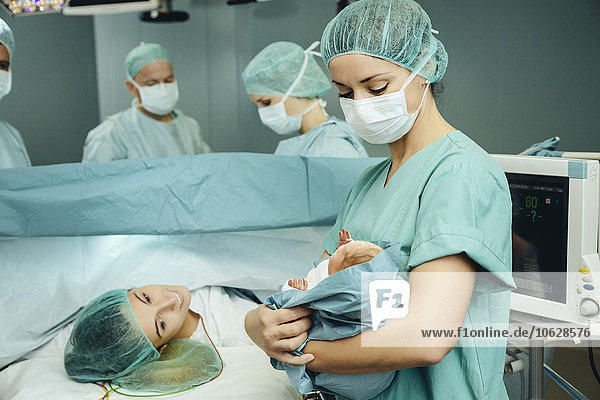 Operationsschwester zeigt Neugeborenes zur Mutter