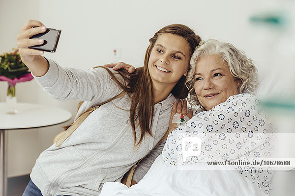 Granddaughter visiting grandmother in hospital  taking selfie with smart phone