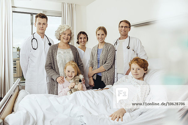 Doctors and famiy in hospital standing by bed of sick boy