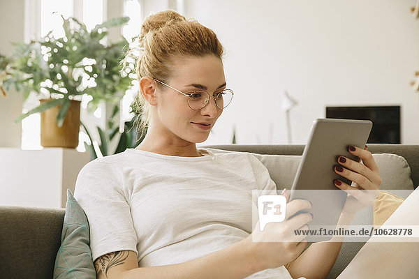 Junge Frau zu Hause  die auf ein digitales Tablett schaut