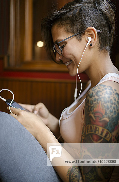 Tattooed young woman listening music with earphones