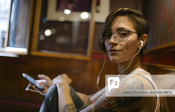 Portrait of tattooed young woman listening music with earphones