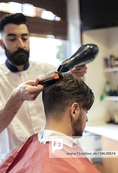 Barber blow-drying and brushing hair of a customer