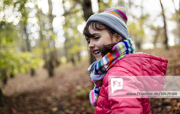Glückliches kleines Mädchen im Wald mit Mütze und Schal im Herbst