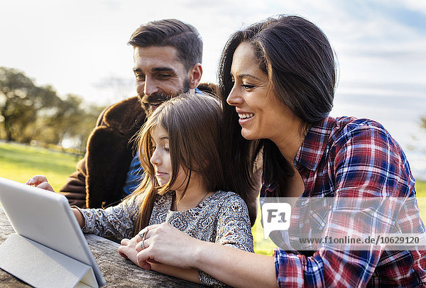 Happy parents with daughter using digital tablet outdoors