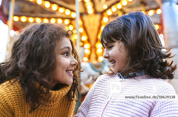 Zwei kleine Mädchen von Angesicht zu Angesicht vor einem Karussell
