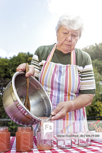 Seniorin gießt hausgemachtes Apfelmus in Marmeladengläser