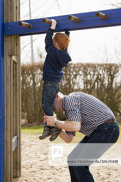 Vater hilft dem Sohn auf dem Spielplatz beim Klettern in der Kletterhalle.