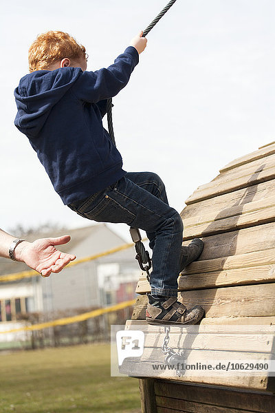 Junge auf dem Spielplatz mit helfender Hand an seiner Seite