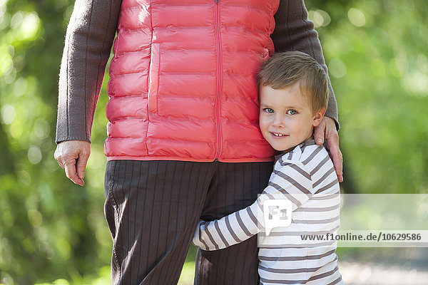 Porträt eines lächelnden kleinen Jungen  der das Bein seiner Großmutter umarmt.