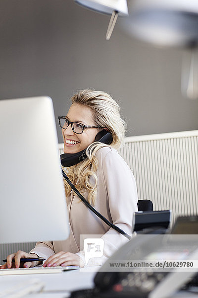 Smiling blond woman in office on the phone