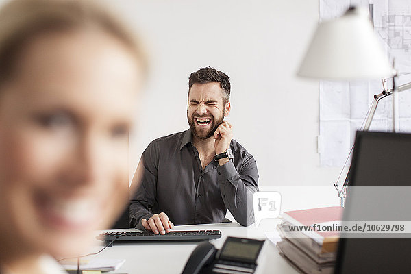 Man in office screaming at desk with woman in foreground