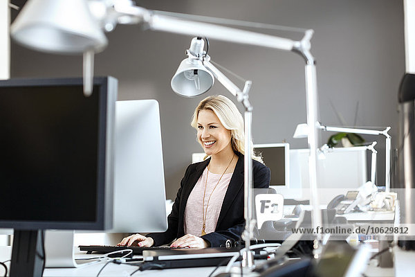 Lächelnde blonde Frau bei der Arbeit am Schreibtisch im Büro