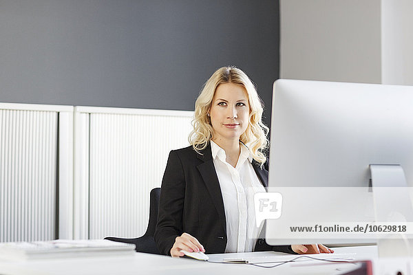 Porträt einer blonden Frau am Schreibtisch im Büro