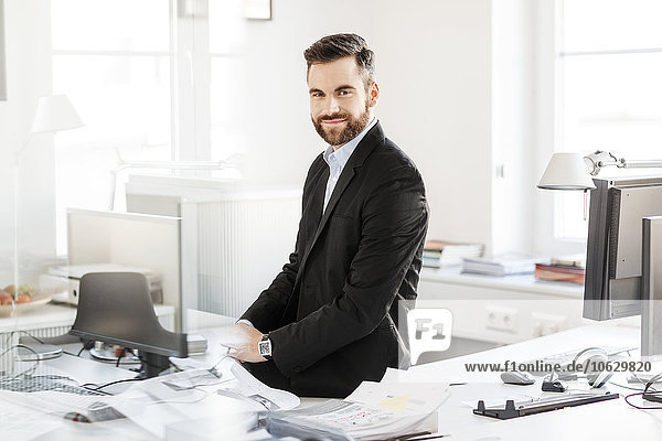 Smiling businessman sitting on desk in office