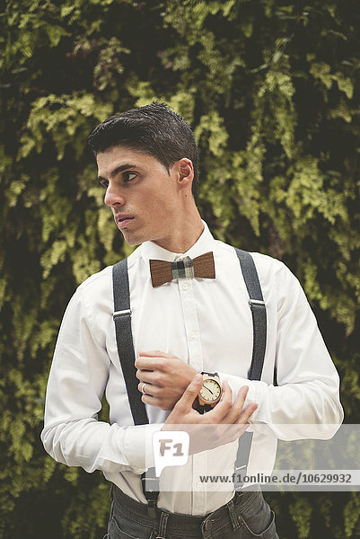 Portrait of elegant young man wearing wrist watch and a wooden bow tie