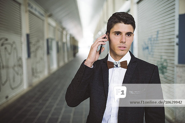 Young man on the phone wearing jacket and a wooden bow tie