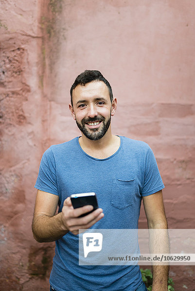 Porträt eines lächelnden bärtigen Mannes mit Smartphone