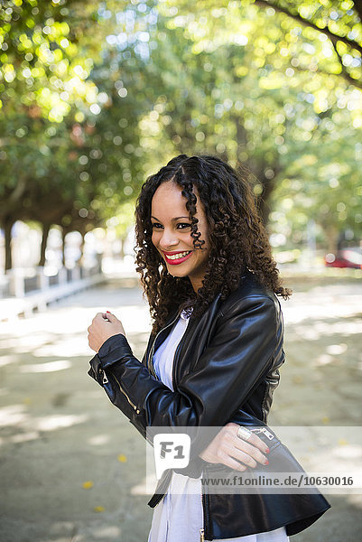 Portrait of smiling young woman with brown ringlets wearing black leather jacket