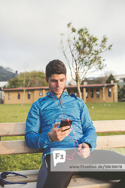 Athlet sitzt nach dem Training auf der Bank und hört Musik vom Smartphone.