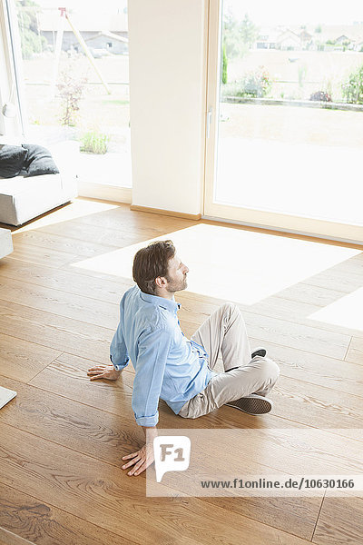 Mature man sitting at home on wooden floor  contemplating