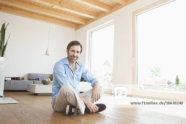 Mature man sitting at home on wooden floor  looking at camera