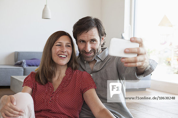 Erwachsenes Paar  das auf dem Boden sitzt und Selfie mit Smartphone nimmt.