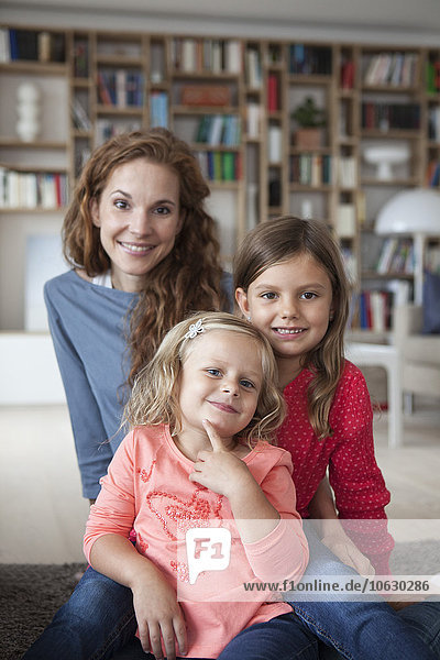 Porträt von zwei kleinen Schwestern und ihrer Mutter im Hintergrund  die im Wohnzimmer auf dem Boden sitzen.