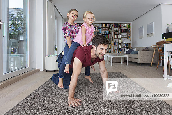Mann der mit seinen kleinen Töchtern im Wohnzimmer spielt.