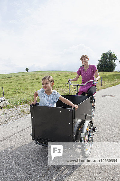 Mother riding bicycle with daughter in trailer