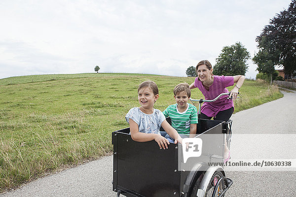 Mother riding bicycle with son and daughter in trailer