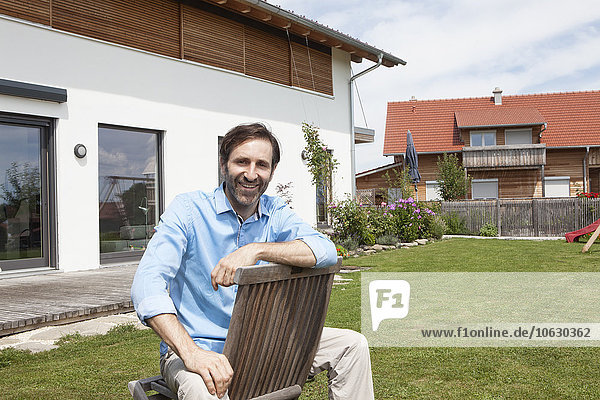 Porträt eines lächelnden Mannes  der auf einem Stuhl im Garten sitzt.