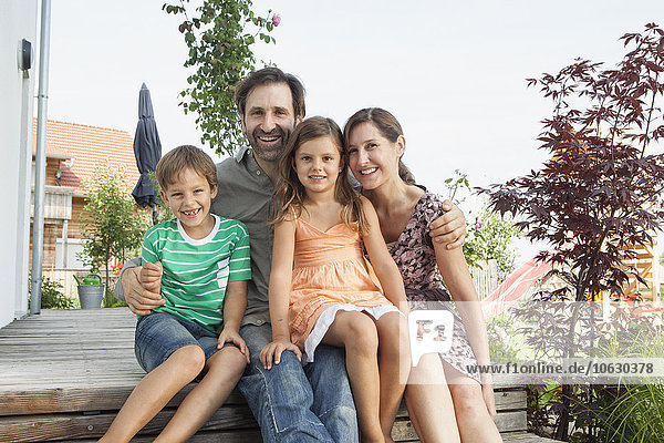 Portrait of smiling family of four sitting on terrace