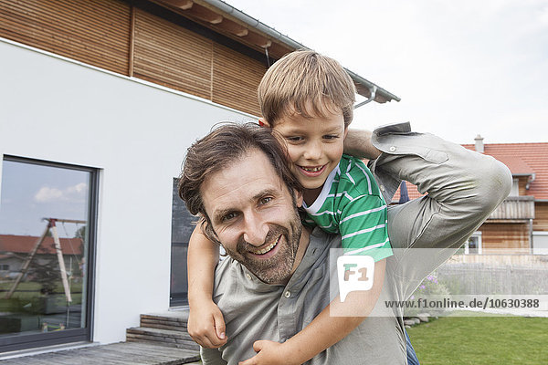 Portrait of happy father carrying son in garden