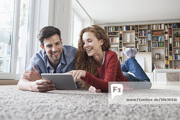 Glückliches Paar auf dem Boden liegend mit digitalem Tablett