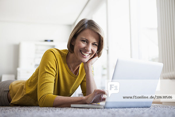 Relaxed woman at home lying on floor using laptop