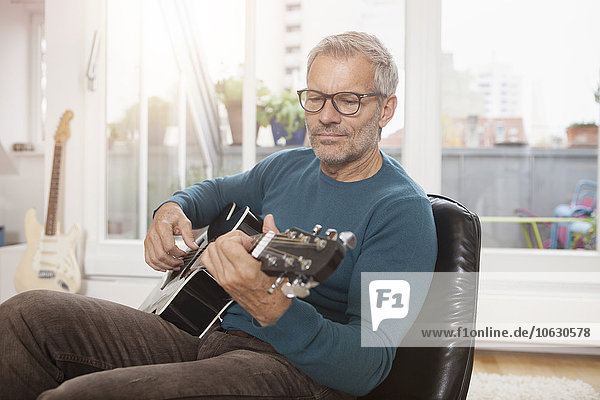 Mature man at home sitting in chair playing guitar