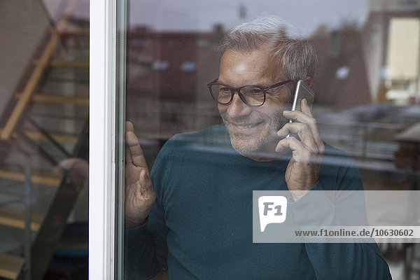 Lächelnder Mann hinter der Fensterscheibe auf dem Handy