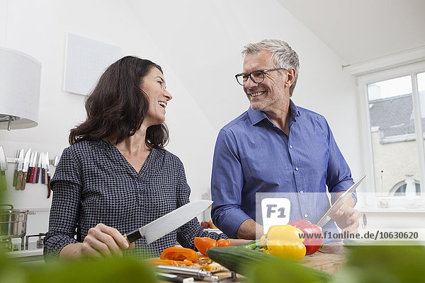 Mature couple with digital tablet cooking in kitchen