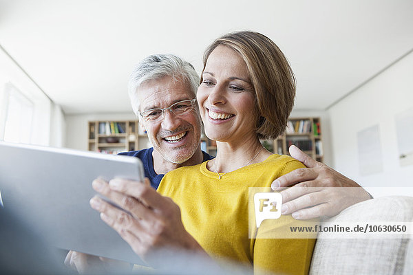 Lächelndes Paar  das zu Hause auf der Couch sitzt und ein digitales Tablett benutzt.