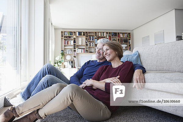 Ein glückliches Paar sitzt Seite an Seite auf dem Boden seines Wohnzimmers.