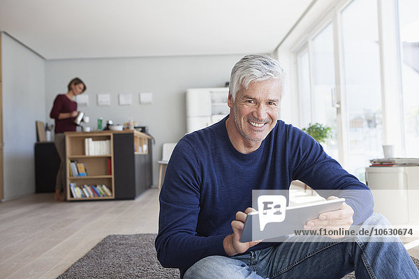 Portrait of smiling man sitting on the floor at home with digital tablet