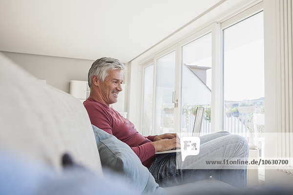 Smiling man sitting on the couch at home using digital tablet